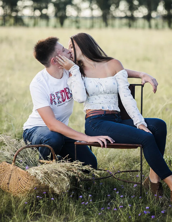 Young couple kisses in sunlit field, surrounded by romantic nature.
