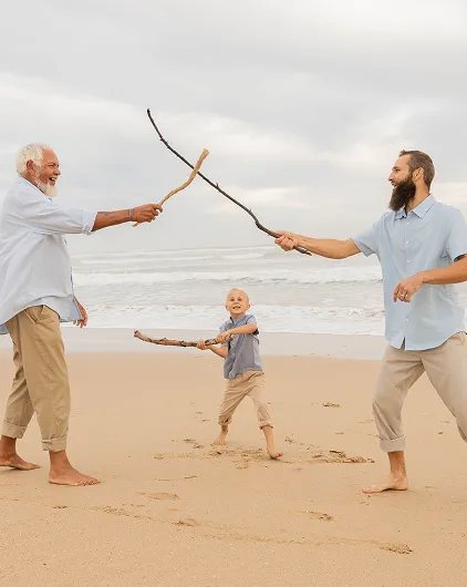 Three generations playfully bond with sticks on a peaceful beach.