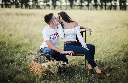 Young couple kisses in sunlit field, surrounded by romantic nature.